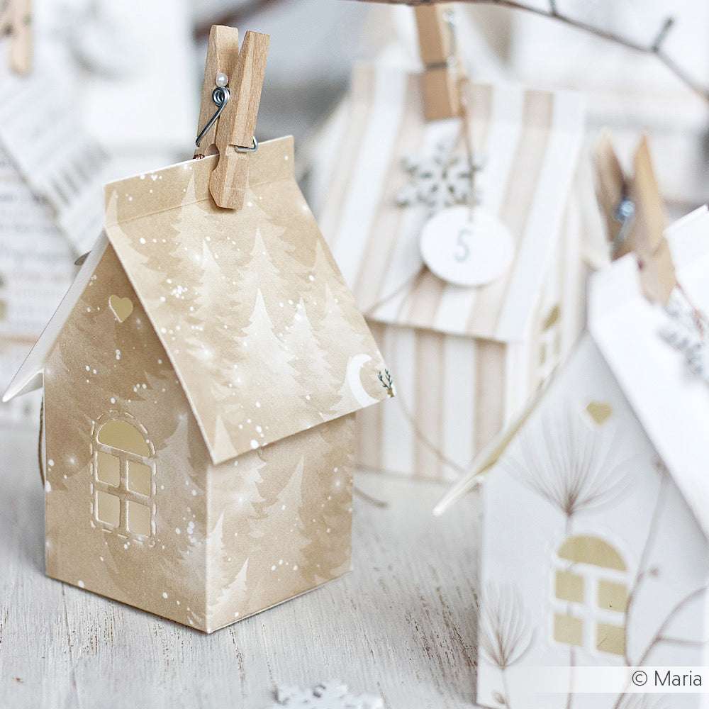 Papierhäuser aus Alexandra Renke Designpapier mit winterlichen Motiven und Wäscheklammern auf einer hellen Holzunterlage - ideal für kreative Papierprojekte oder um Winterwald-Feeling in die Weihnachtsdekoration zu bringen.