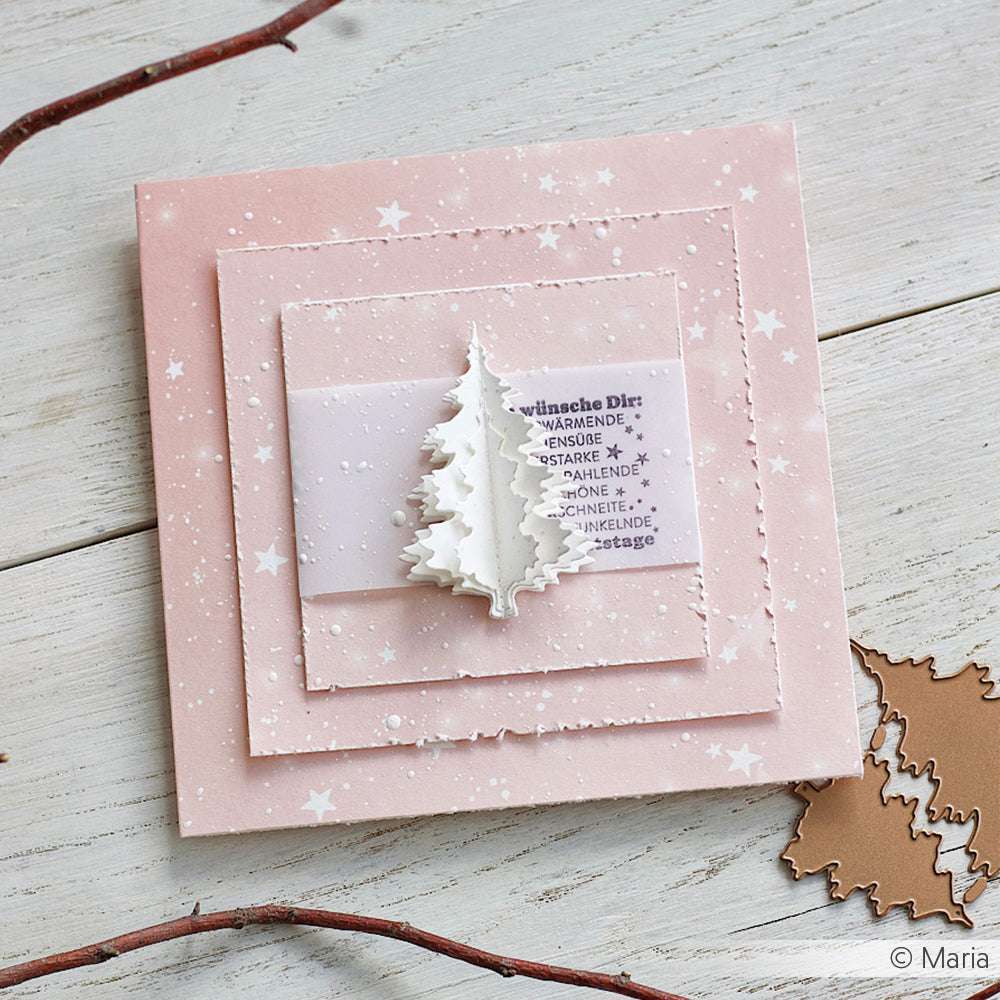 Quadratische rosafarbene Weihnachtskarte von Alexandra Renke aus Bastelpapier mit einem weißen 3D-Baum mit deutschem Text, der auf einer hölzernen Fläche mit Zweigen in der Nähe steht.