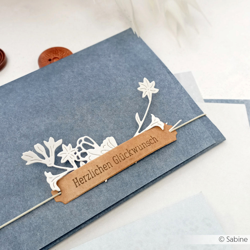 Blauer Umschlag mit floralem Ausschnitt aus hochwertigem Designpapier von Alexandra Renke, veredelt mit einem braunen Etikett mit der Aufschrift "Herzlichen Glückwunsch" in Deutsch. Ideal für Buchbinderei oder ausgefallene Papierprojekte.
