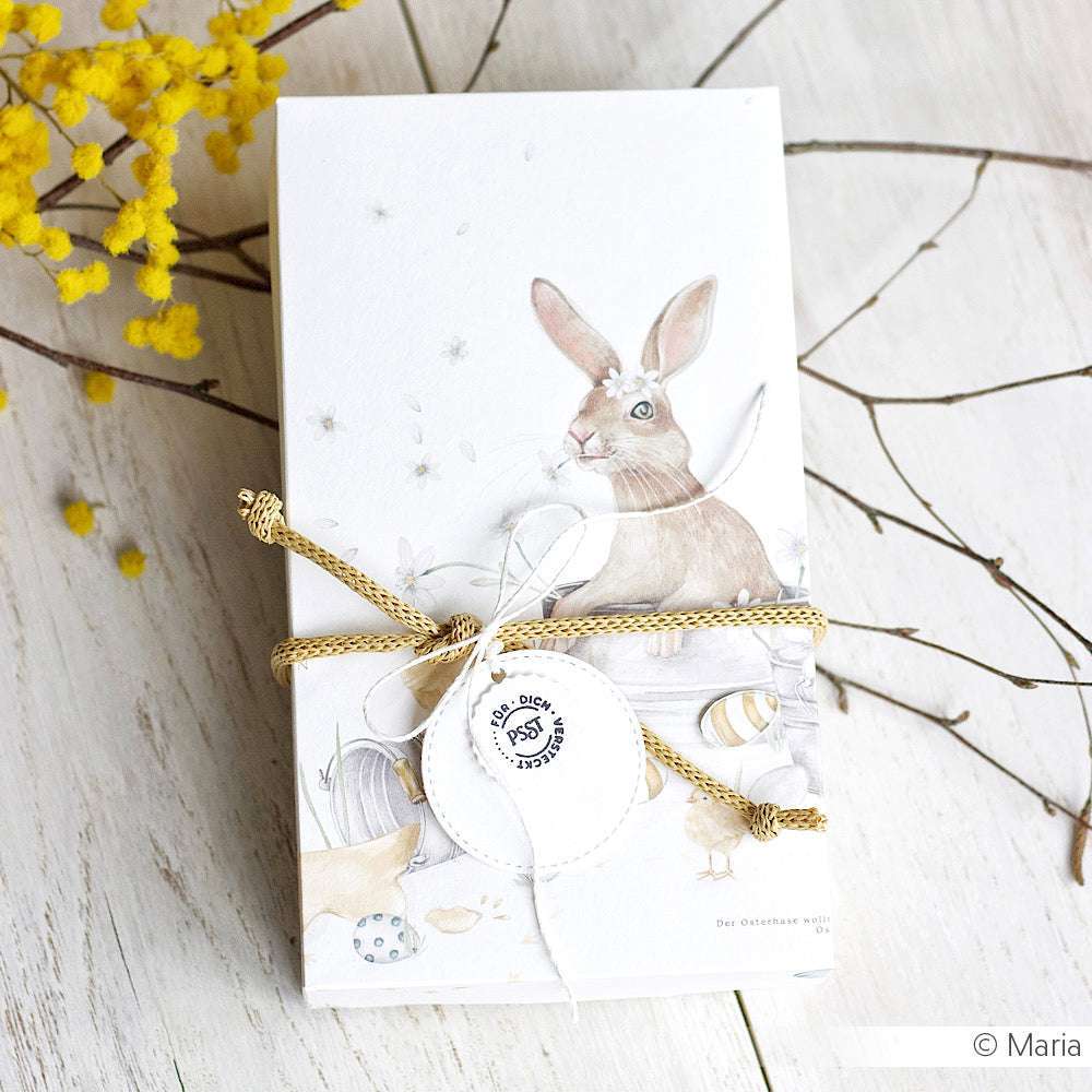 Eine Karte von Alexandra Renke aus Designpapier zeigt ein Kaninchen, Eier und eine Schnur auf Holz mit gelben Blumen und Zweigen - die perfekte Inspiration für Grußkarten oder Papierprojekte.