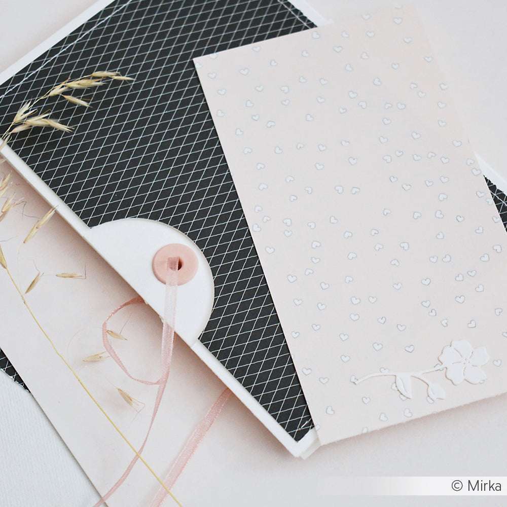 Eine hellrosa Blumenkarte sitzt auf einem schwarz gemusterten Umschlag, der mit hochwertigem Designpapier von Alexandra Renke gefertigt wurde - ideal für die Buchbinderei oder besondere Papierprojekte - und mit einem charmanten Knopf- und Schleifenverschluss versehen ist.