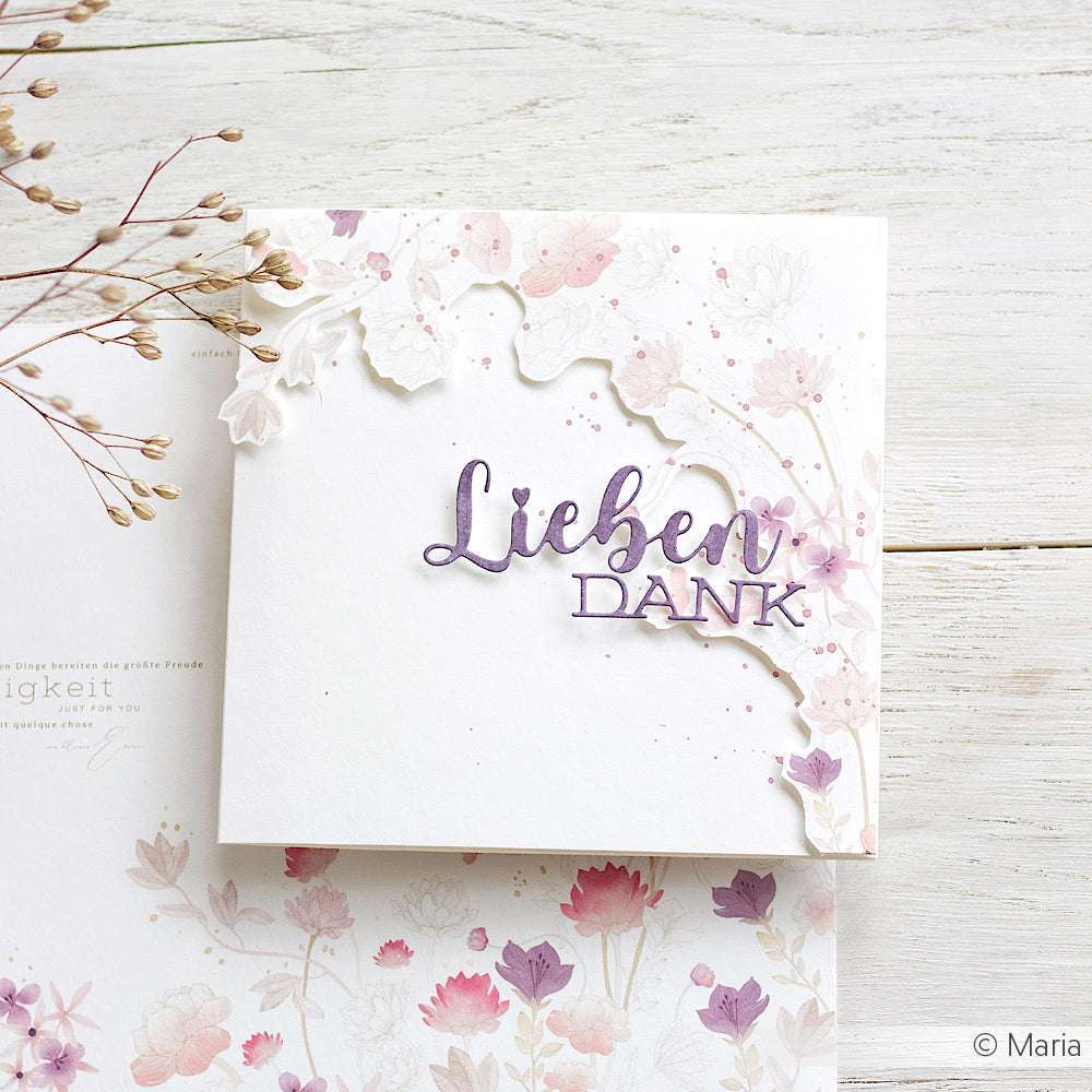 Eine Blumenkarte von Alexandra Renke mit "Lieben DANK" in Lila, umgeben von pastellfarbenen Blumen auf weißem Holz - ideal für Papierprojekte oder um Ihrer Designpapier-Sammlung einen handgemachten Touch zu verleihen.