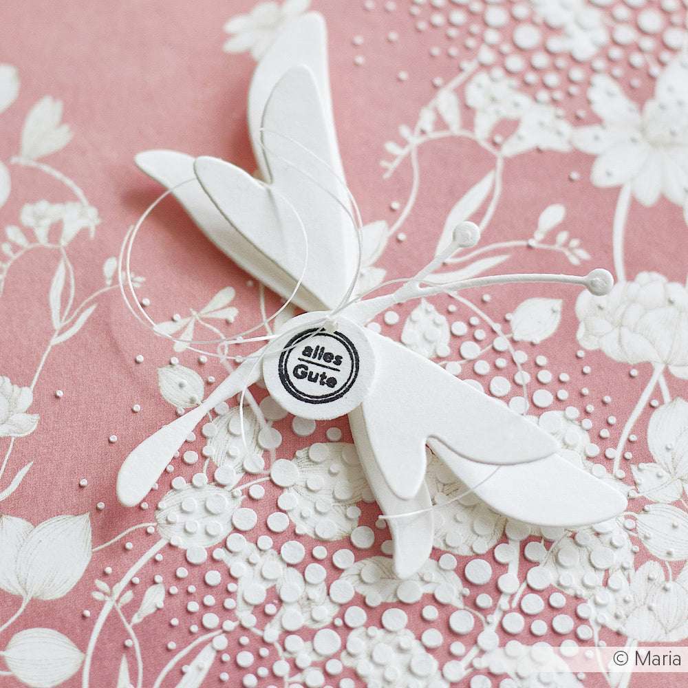 Weißer Papierschmetterling mit "Alles Gute"-Button auf rosafarbenem Blumenhintergrund von Alexandra Renke - ideal für Papierprojekte oder zum Basteln mit Designpapier. Eine schöne weiße Blumenvariation bereichert die zarte Szene.