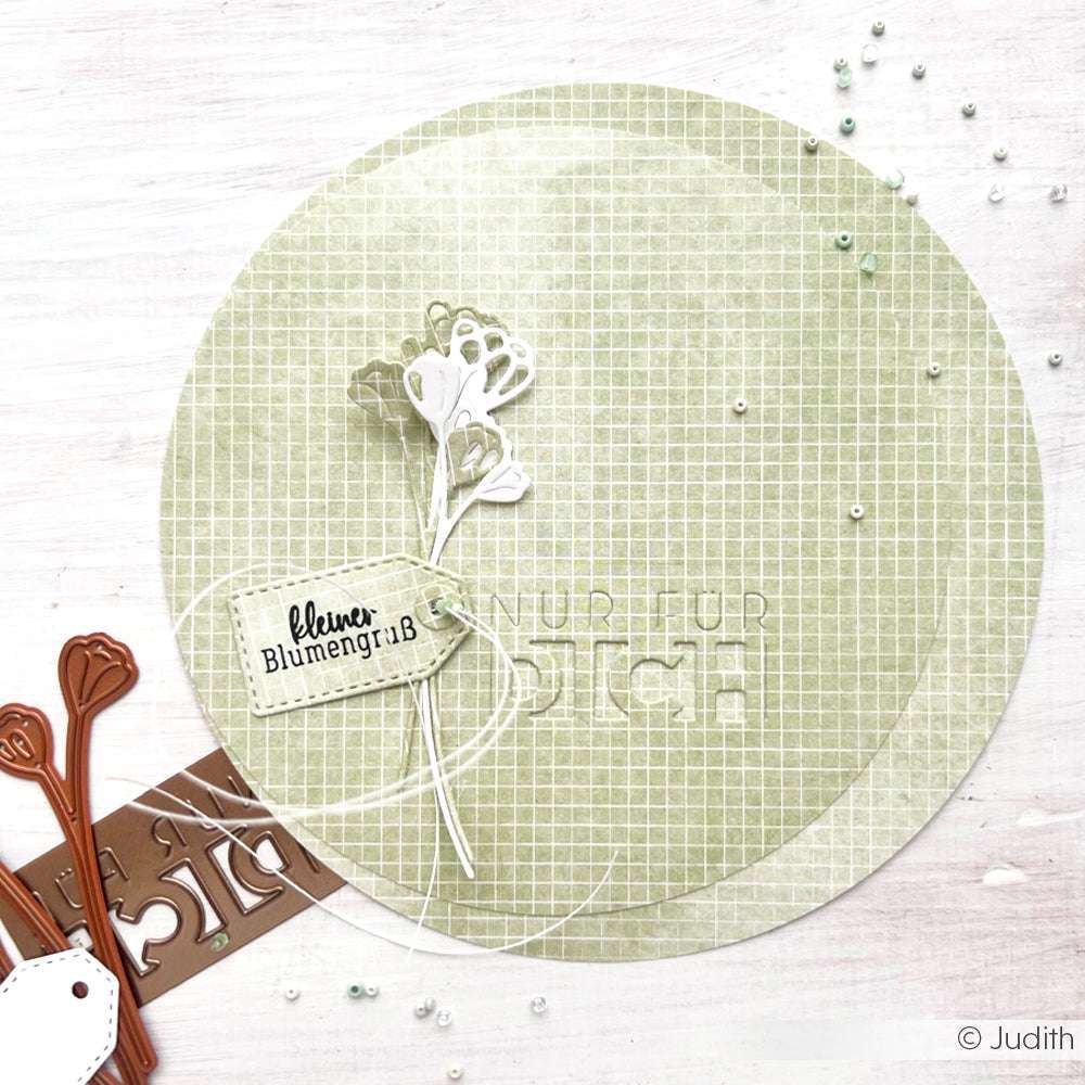 Eine Karte mit grünem Gittermuster, weißer Blume und "kleinem Blumengruß" von Alexandra Renke sowie Stanzwerkzeugen aus Metall - ideal für Papierprojekte oder zur Verschönerung der Buchbinderei.