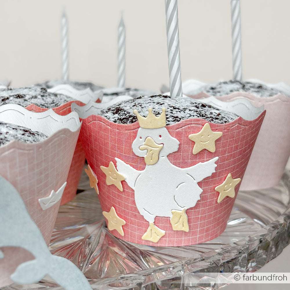 Schokoladen-Cupcake in rosa Verpackung aus Alexandra Renke Mimi Korallenrot Designpapier, verziert mit einer gekrönten Ente und gelben Sternen auf einem Glastablett - ein idealer Akzent für Ihre Papierprojekte.