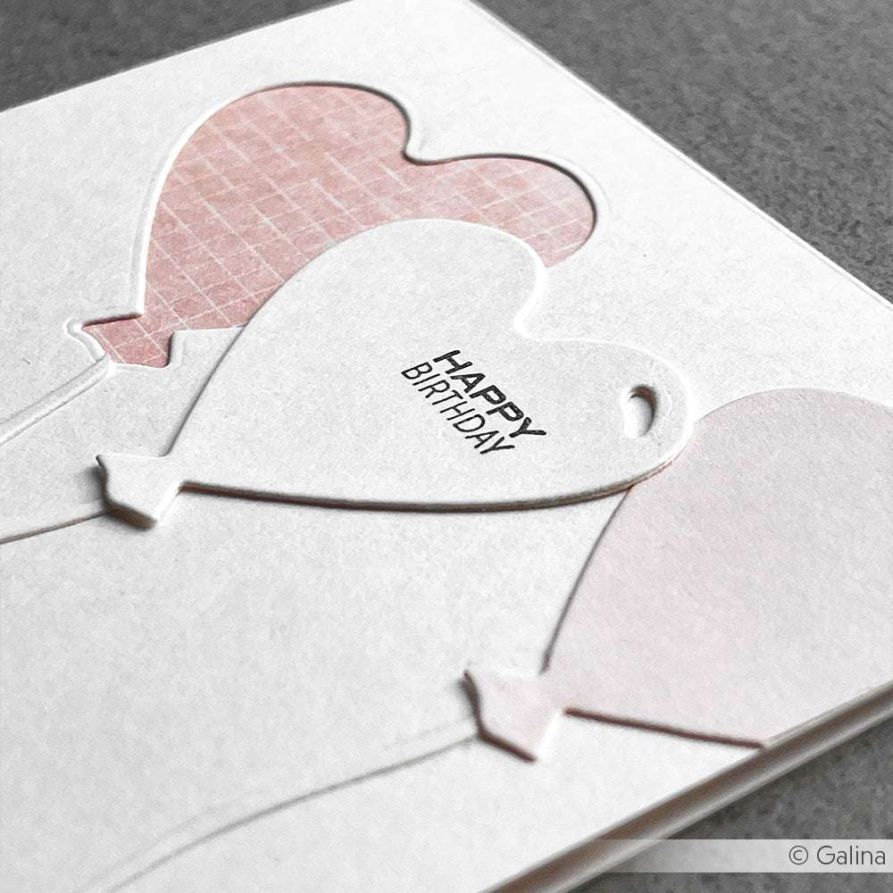 Nahaufnahme einer weißen Geburtstagskarte von Alexandra Renke mit drei herzförmigen Ballonmotiven auf Designpapier und dem Text "Happy Birthday".