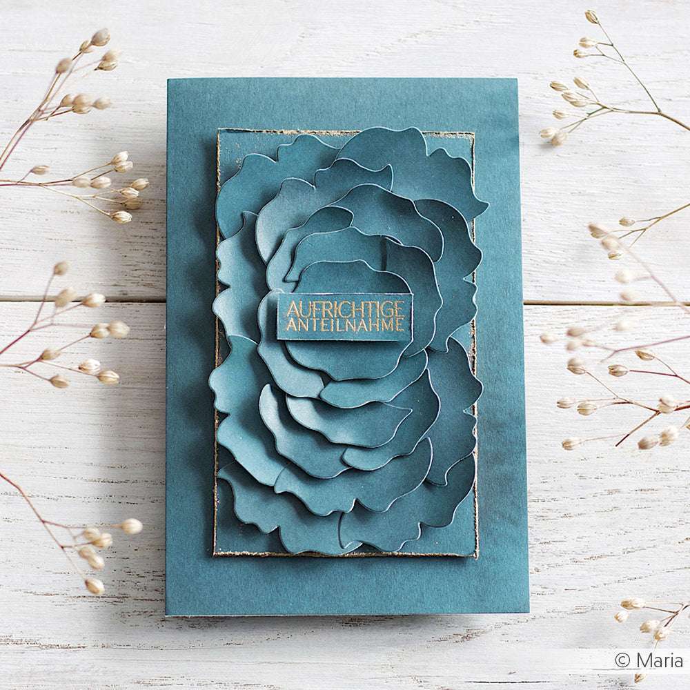 Eine tealfarbene Beileidskarte von Alexandra Renke, die mit Bastelpapier hergestellt wurde, zeigt eine geschichtete Blume und "AUFRICHTIGE ANTEILNAHME" in Gold auf einer weißen Holzoberfläche.