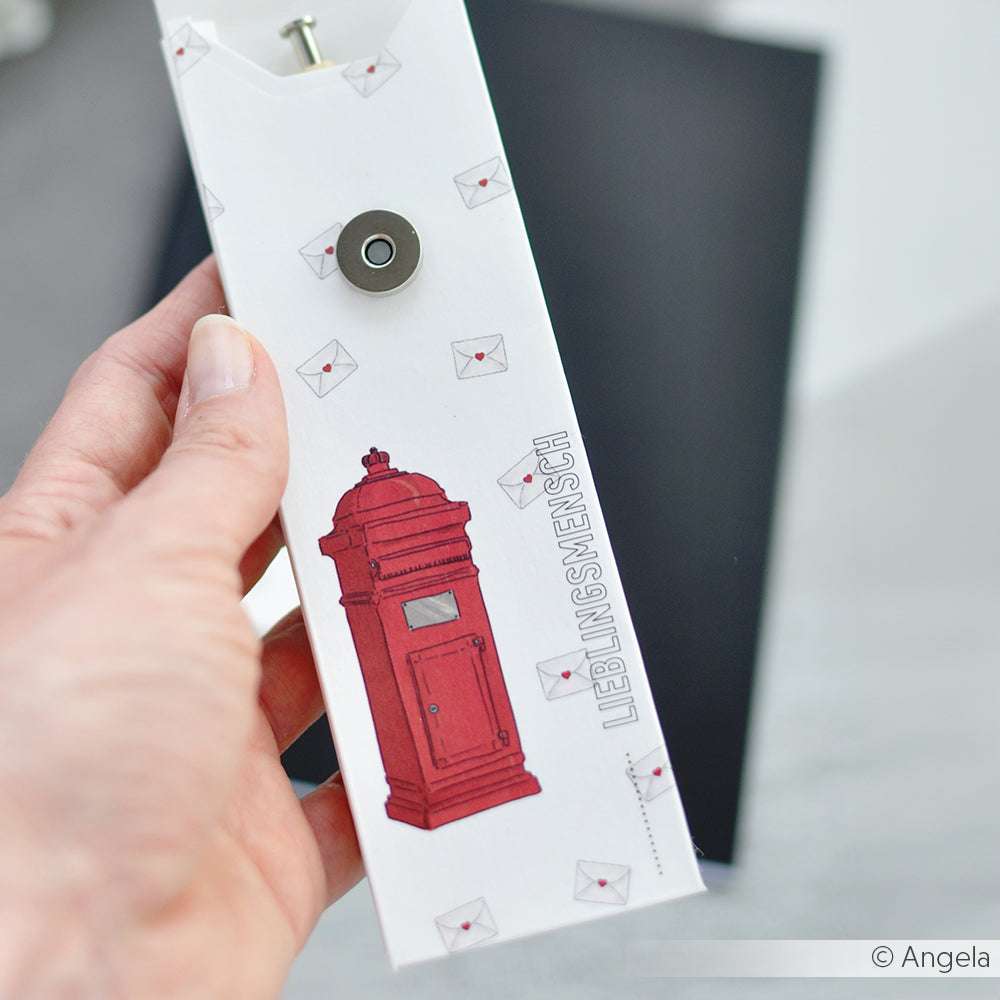 Eine Hand hält einen weißen Umschlag von Alexandra Renke aus hochwertigem Designpapier mit rotem Briefkasten und dem Schriftzug LIEBLINGSMENSCH - ideal für Papercraft-Projekte oder zum Buchbinden.