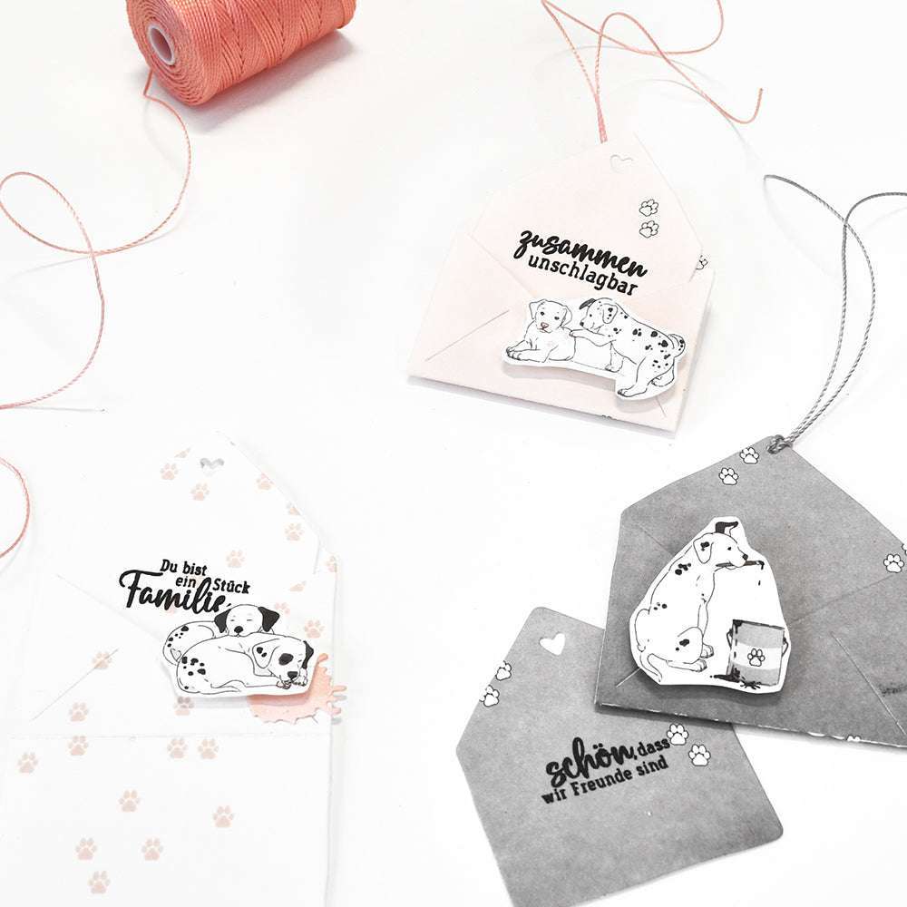 Set mit vier verzierten Briefumschlägen von Alexandra Renke mit Hunde-Illustrationen, deutschem Text und rosa Kordel auf weißem Hintergrund - ideal für Papierprojekte oder das Versenden von unverwechselbaren Grußkarten.