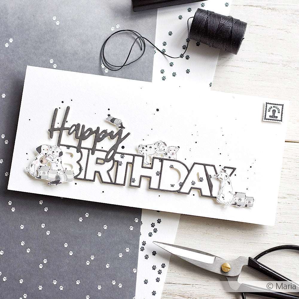 Handgemachte Happy-Birthday-Karte von Alexandra Renke mit silbernen Akzenten, Schere, schwarzem Faden und Designpapier mit Pfotenabdruck auf einem Schreibtisch - eine reizvolle Option für Ihre nächsten Papierprojekte.