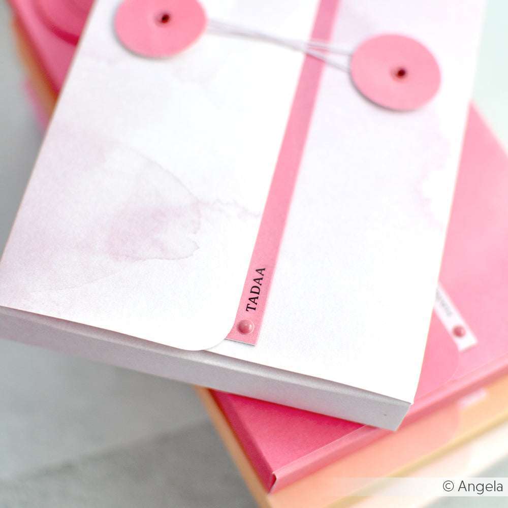 Nahaufnahme eines rosafarbenen Umschlags mit Kordelzug und dem Text "TADAA", gestapelt auf bunten Umschlägen - perfekt für Papierprojekte, hergestellt mit Rosa-Pink Verlauf Designpapier von Alexandra Renke.