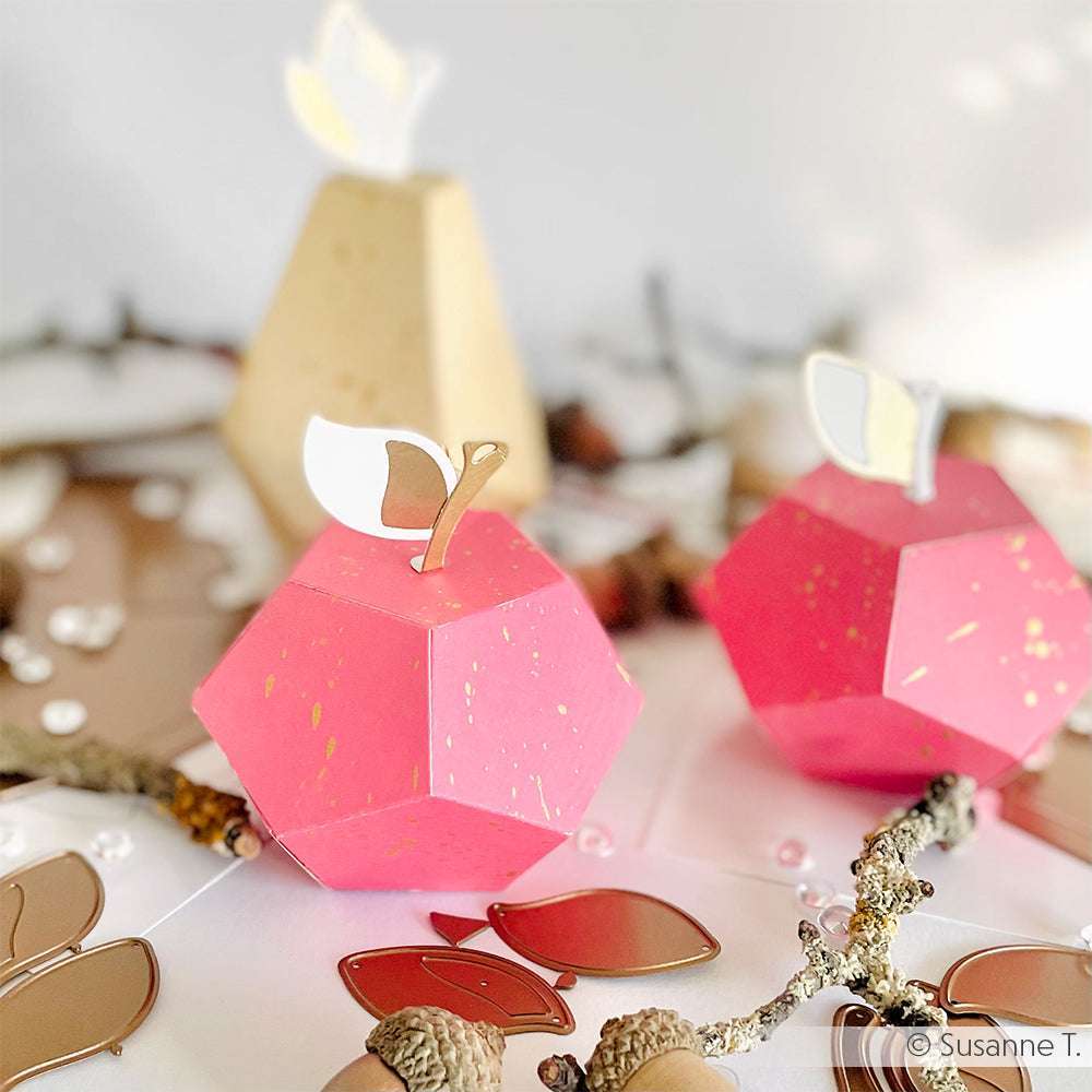 Zwei rosafarbene, geometrische Papierarbeiten in Form von Äpfeln, hergestellt mit dem Pink-Lila-Verlauf Designpapier von Alexandra Renke, mit goldenen Stielen und weißen Blättern, umgeben von dekorativen Akzenten.