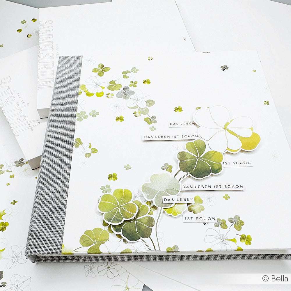 Ein Scrapbook von Alexandra Renke mit Glücksklee Designpapier, Kleemustern und "Das Leben ist schön" auf einem weiß-grauen Einband - ideal für Papierprojekte.