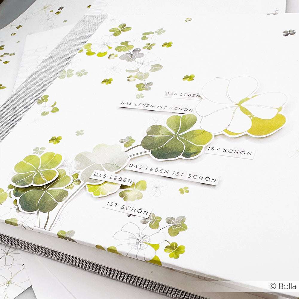 Ein Bogen von Alexandra Renke Designpapier mit grünen Kleemotiven und deutschem Text: Das Leben ist schön.