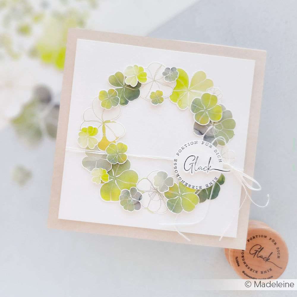 Die handgefertigte Karte von Alexandra Renke zeigt einen grünen Kleekranz von Designpapier, einen runden Glücksanhänger und ist mit weißer Schnur gebunden - perfekt für Papierprojekte.