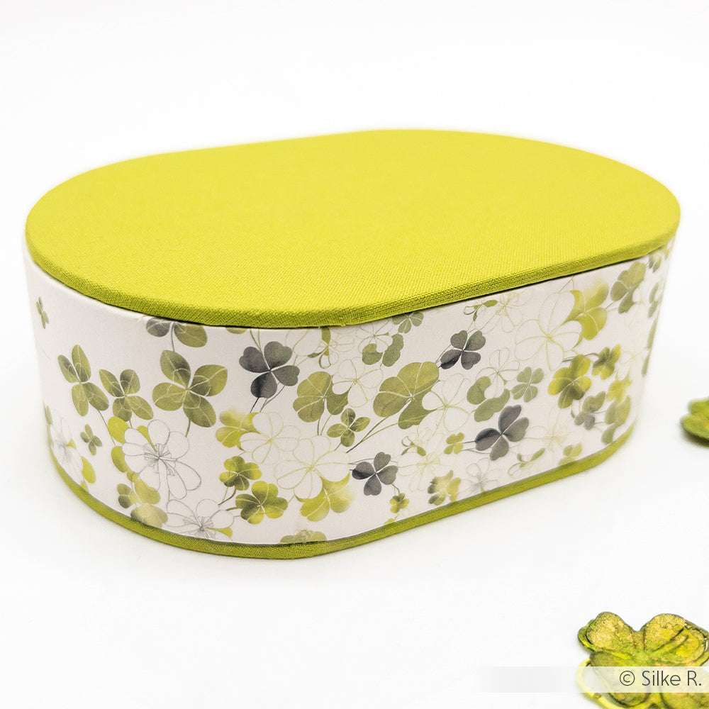 Ovale Schachtel von Alexandra Renke mit grünem Deckel und kleeblattgemusterten Seiten, ideal zur Aufbewahrung von Grußkarten oder Papierprojekten, abgebildet auf weißem Hintergrund.