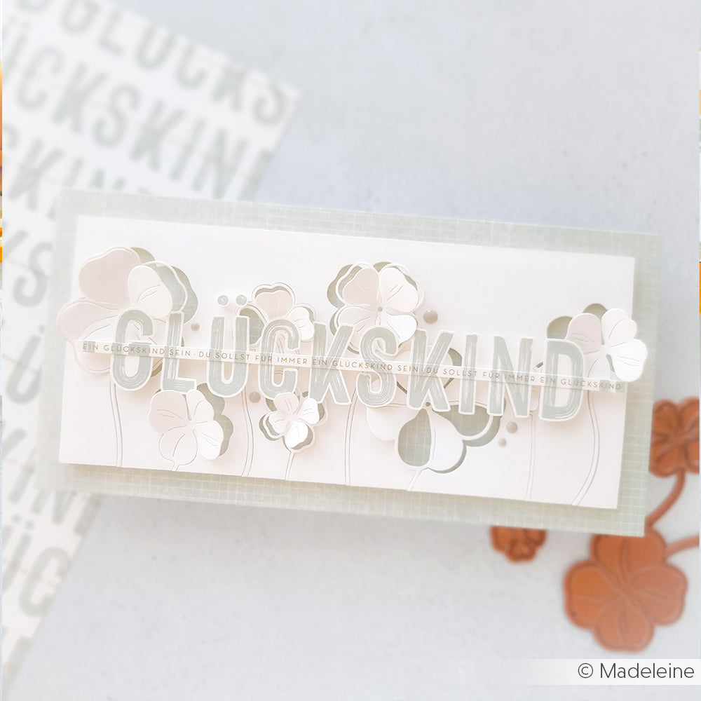 Eine handgefertigte Grußkarte von Alexandra Renke mit floralen Ausschnitten, gefertigt aus hochwertigem Designpapier, mit GLÜCKSKIND in Fettdruck auf hellem Grund.