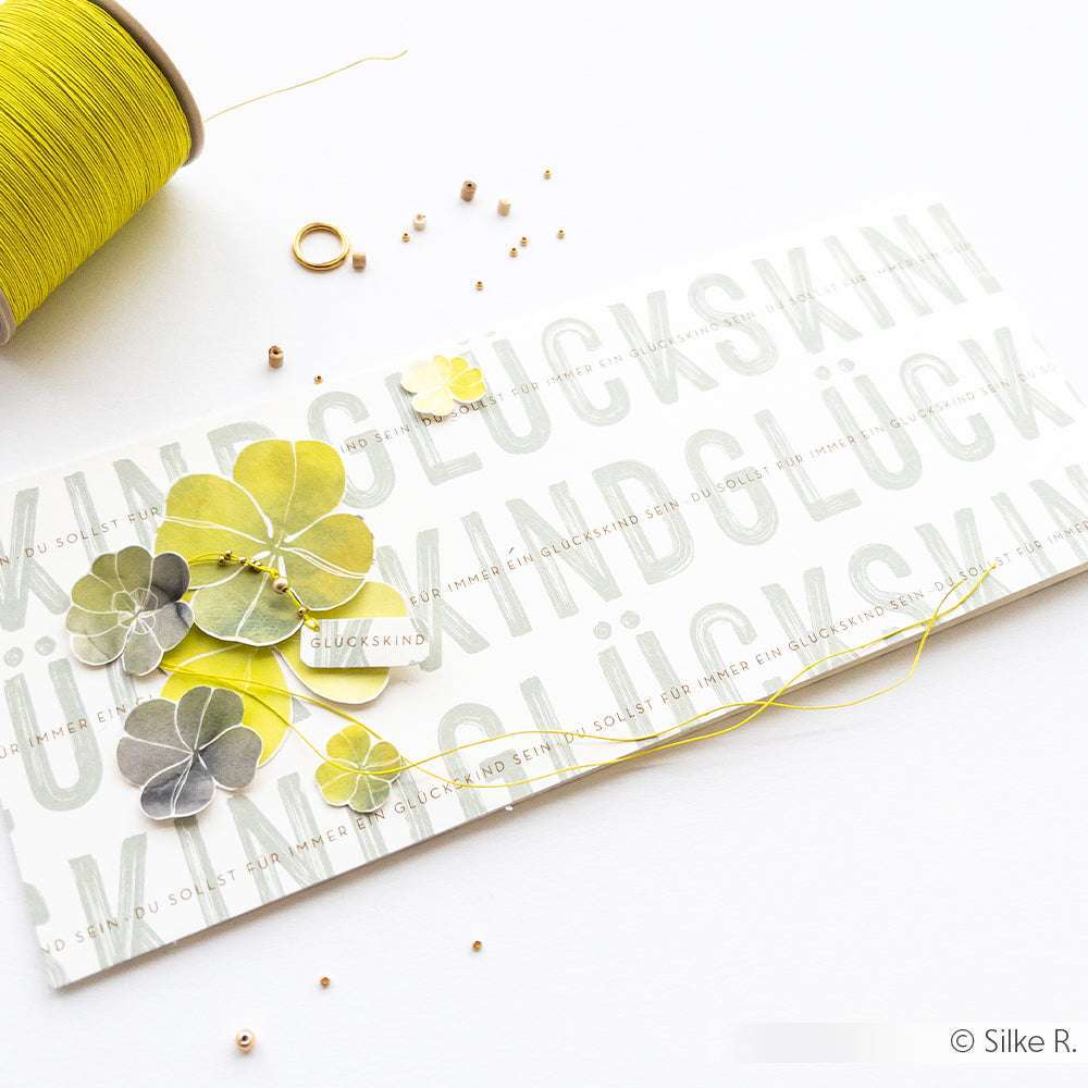 Handgefertigte Grußkarten von Alexandra Renke mit Papierkleeblättern, gelbem Faden und Perlen auf weißem Grund - ideal für Papierprojekte oder alle, die einzigartiges Designpapier lieben.