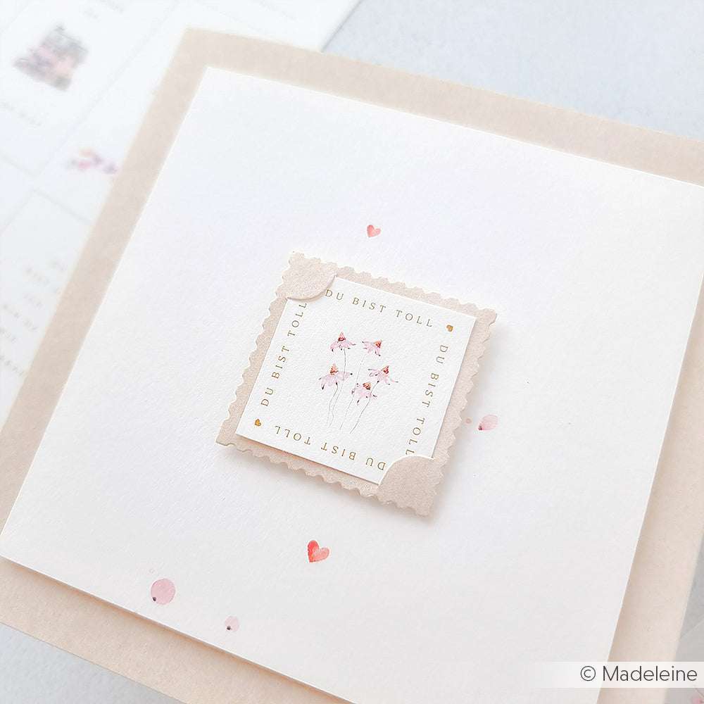 Eine quadratische Karte von Alexandra Renke mit einem zarten Stempelmotiv, rosa Blüten aus der Serie Zarte Blütenwiese und kleinen roten Herzen auf weißem Designpapier.