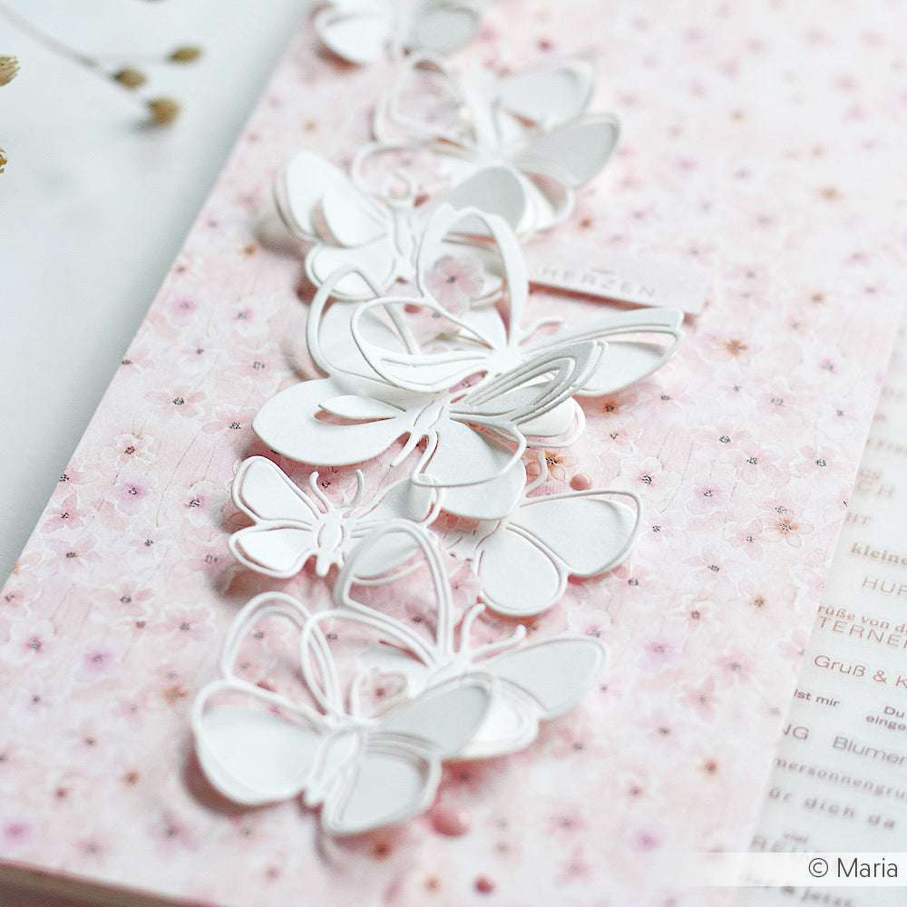 Weiße Papierschmetterlinge zieren eine Karte in Blütenmuster rosa von Alexandra Renke Designpapier mit zarten Ausschneidedetails - ideal für elegante Papierprojekte.