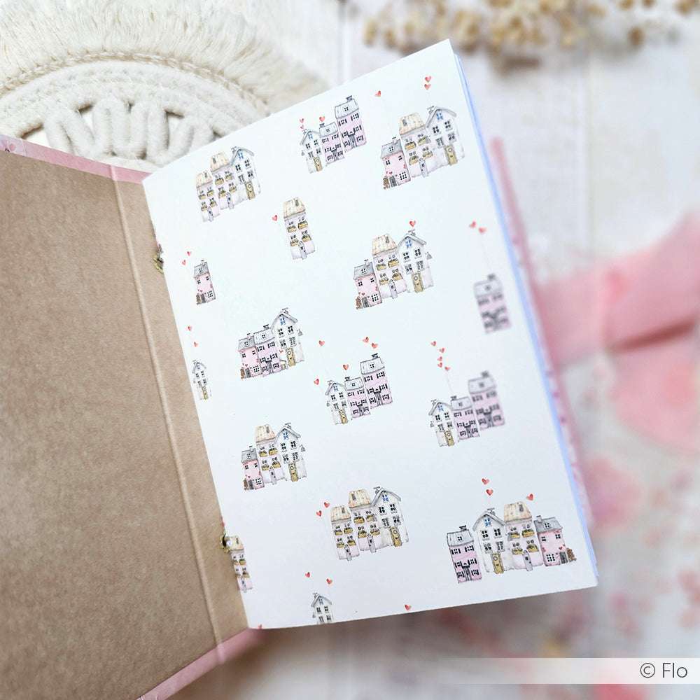 Aufgeschlagenes Notizbuch von Alexandra Renke mit illustrierten Häusern und roten Herzen auf der Innenseite des Einbands, hergestellt mit Buchbinderei-Techniken und charmantem Design-Papier, auf einer leicht strukturierten Oberfläche.