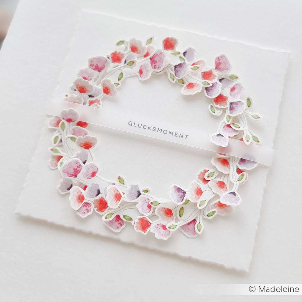 Eine zarte Blumenkranzkarte von Alexandra Renke, gestaltet mit Designpapier, mit rosa und lila Blumen und dem Wort "GLÜCKSMOMENT" in der Mitte.