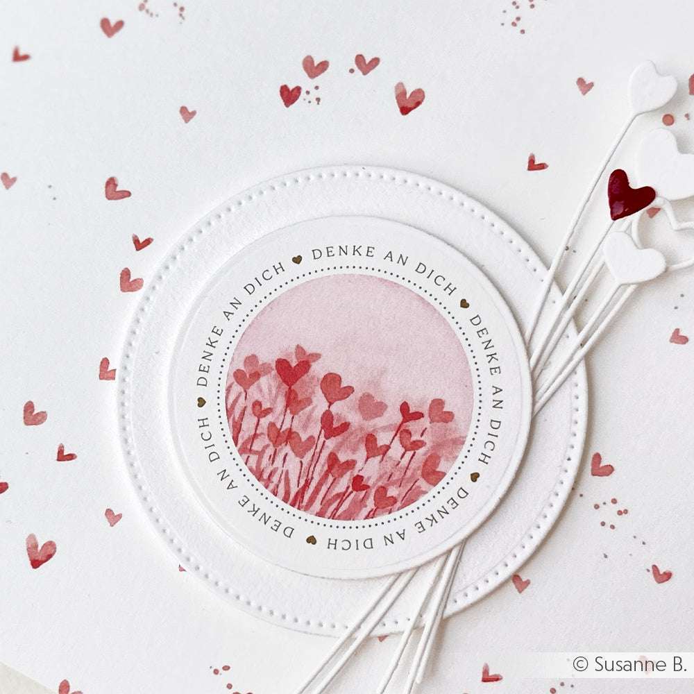 Eine Karte von Alexandra Renke mit rosa und roten Herzen, einer kreisförmigen "Denke an Dich"-Botschaft und herzförmigen Stiften aus Designpapier und dem Kärtchenbogen Feine Blütenwelt - ideal für liebevolle Papierprojekte.