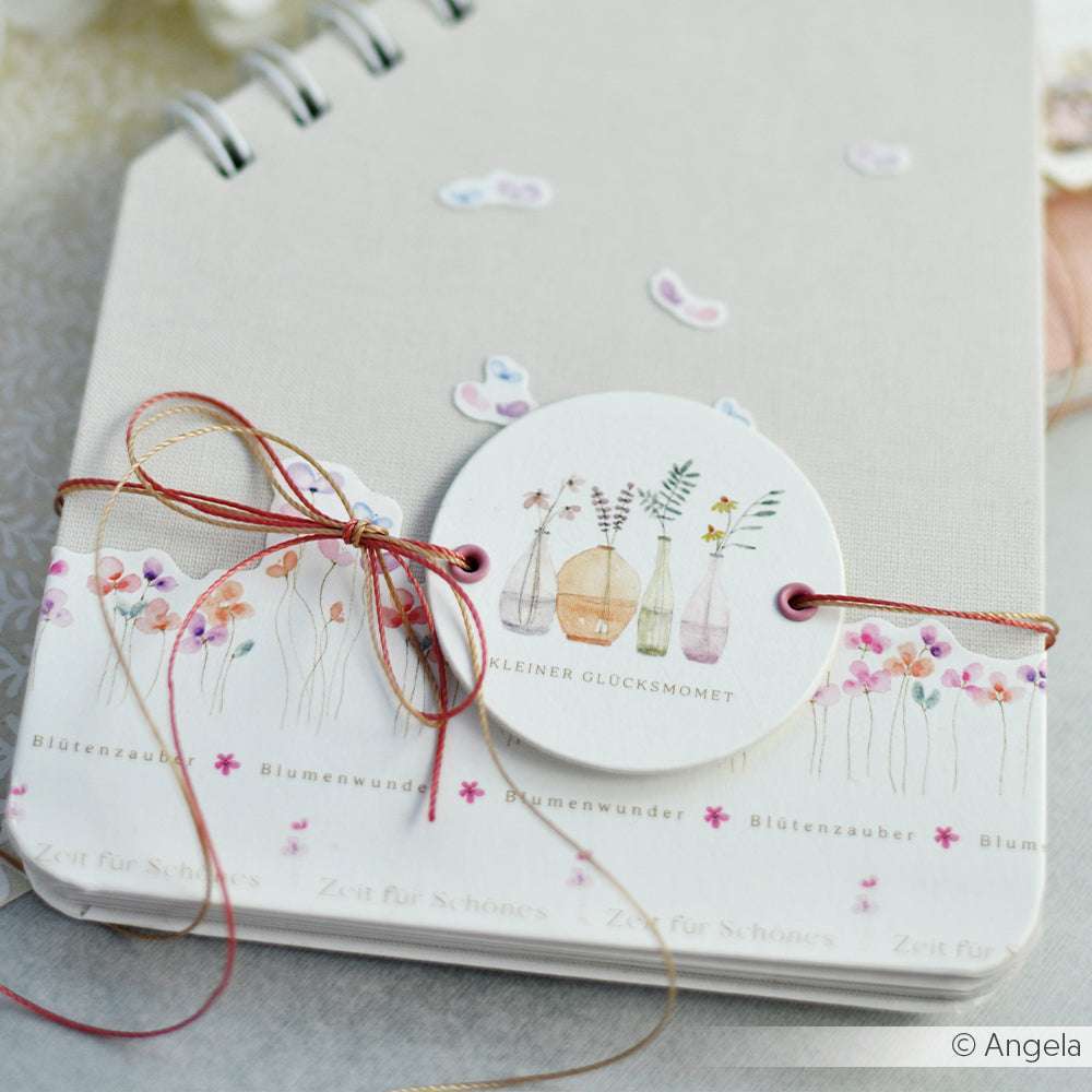 Ein floral illustriertes Notizbuch von Alexandra Renke, gebunden mit Schnur und einem runden Anhänger mit Aquarellvasen und Blumen - ideal für Buchbinderei und kreative Papierprojekte.