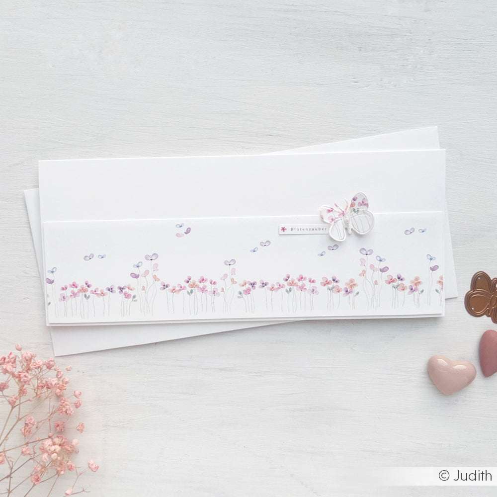 Weiße Karte von Alexandra Renke mit rosa und lila Blumen und einem Schmetterling auf feinem Designpapier. Ideal für kreative Papierprojekte und persönliche Grußkarten; auf einer hellen Oberfläche mit Herzformen verziert.