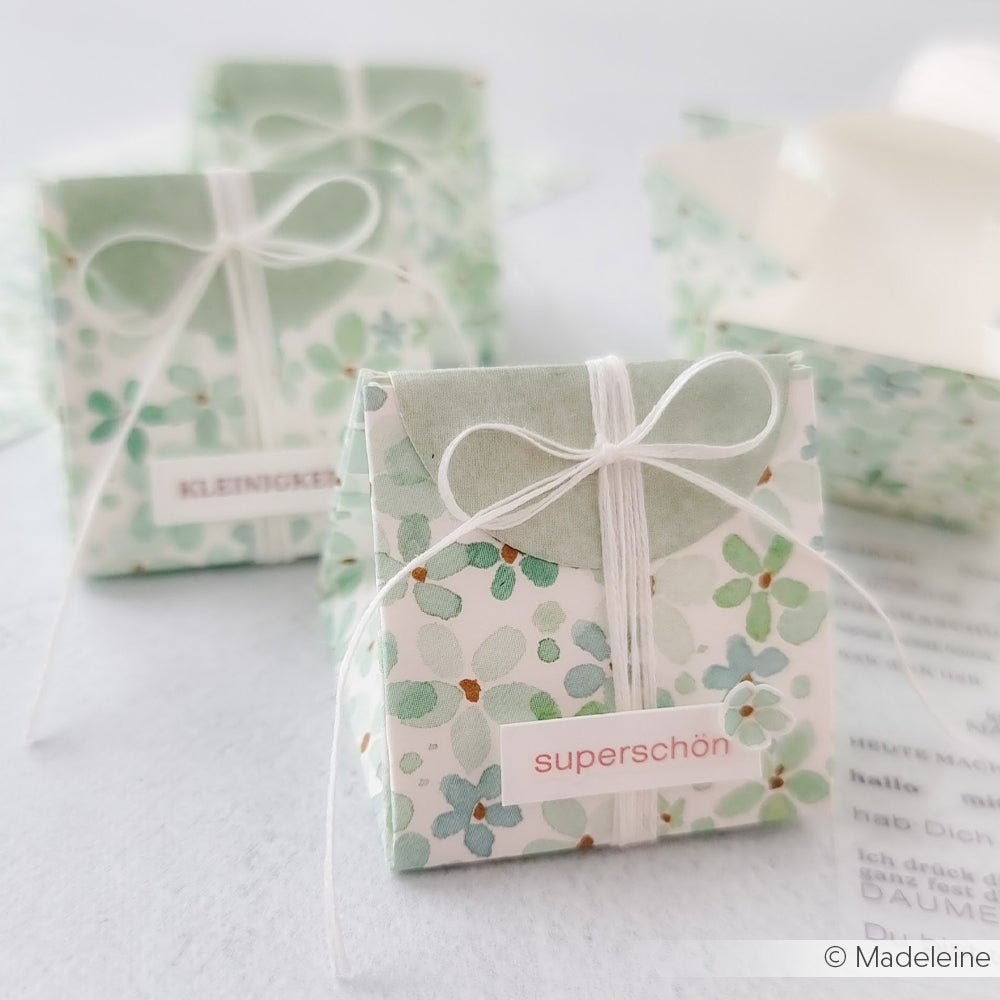 Kleine florale Geschenkboxen aus Alexandra Renke Designpapier Blütenmuster, mit weißer Kordel verschnürt und mit "superschön" und "KLEINIGKEIT" beschriftet - perfekt für Papierprojekte oder als Buchbinderei auf jeder hellen Fläche.