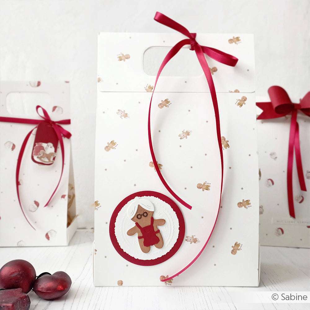 Weiße Geschenktüte von Alexandra Renke mit kleinen Lebkuchenaufdrucken, roter Schleife und einer Lebkuchenfrau auf der Vorderseite - perfekt für die Kombination mit passendem Designpapier oder Grußkarten für eine festliche Präsentation.