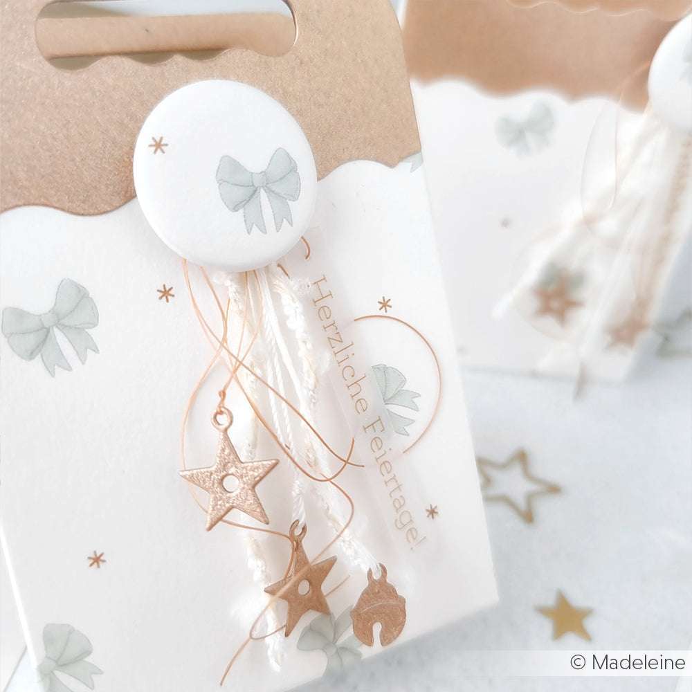 Die weiße Geschenktüte von Alexandra Renke ist mit grünen Schleifen, goldenen Sternchen und "Herzliche Feiertage" verziert - eine festliche Note, die sich perfekt mit Grußkarten kombinieren oder Papierprojekte mit Ihrem Lieblingsdesignpapier aufwerten lässt.