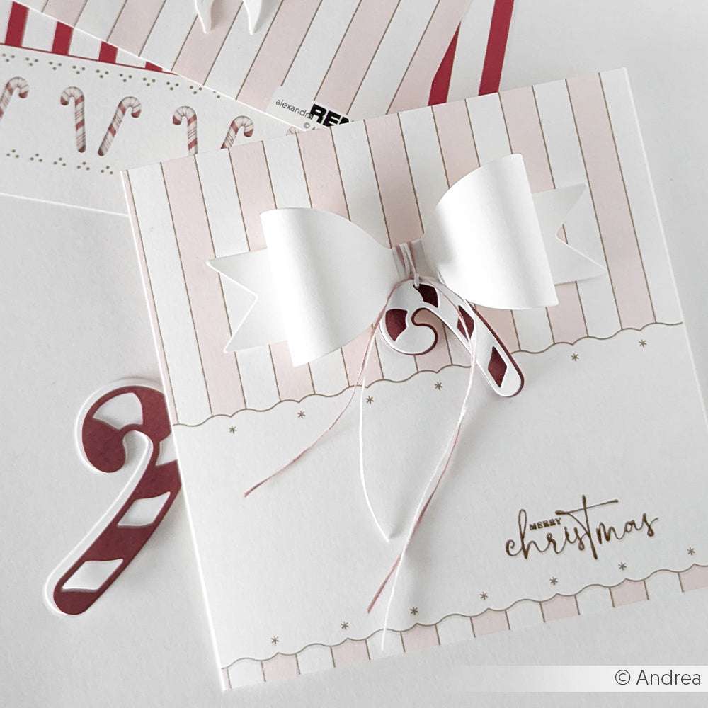Handgemachte Weihnachtskarte von Alexandra Renke aus Designpapier mit weißer Papierschleife, Zuckerstangen-Dekoration, Ornament-Bordüre Rosa und dem Text "Frohe Weihnachten".