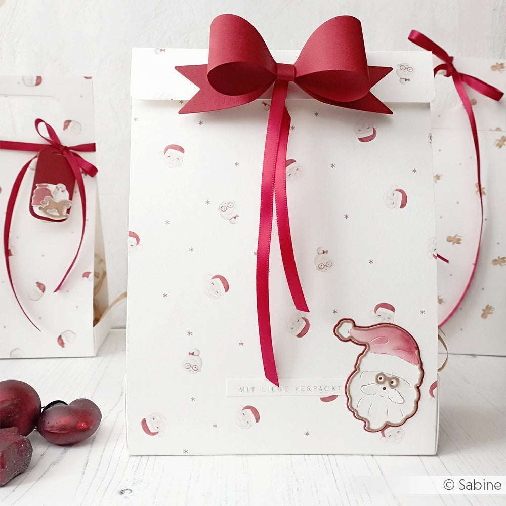 Weiße Geschenktüte mit roter Schleife, Weihnachtsmanngesicht und festlichen roten Ornamenten - perfekt für Papierprojekte oder Designpapier Basteln zu Weihnachten. Von Alexandra Renke.