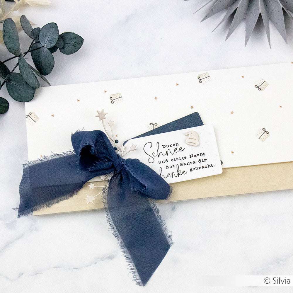 Weiß-goldener Geschenkumschlag von Alexandra Renke mit marineblauer Schleife, festlicher Grußkarte und eleganten Designpapier-Details auf marmoriertem Hintergrund.