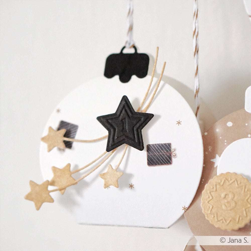 Das runde, hängende Ornament von Alexandra Renke zeigt schwarze und goldene Sterne sowie kleine Geschenkdekorationen auf weißem Hintergrund - ideal für Papierbasteleien oder um Ihren Buchbindeprojekten Stil zu verleihen.