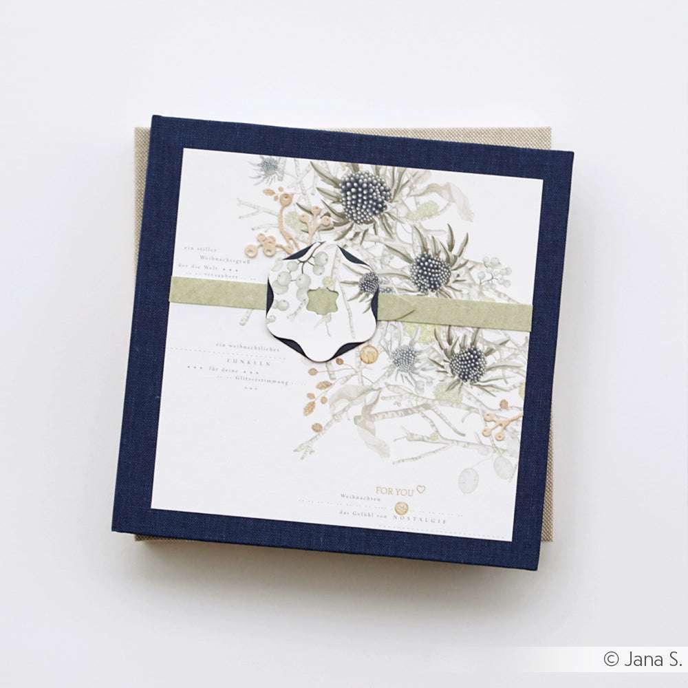 Eine quadratische Grußkarte von Alexandra Renke mit botanischen Illustrationen und einem grünen Band, gefertigt aus feinem Designpapier, steht auf einem hellen Hintergrund.