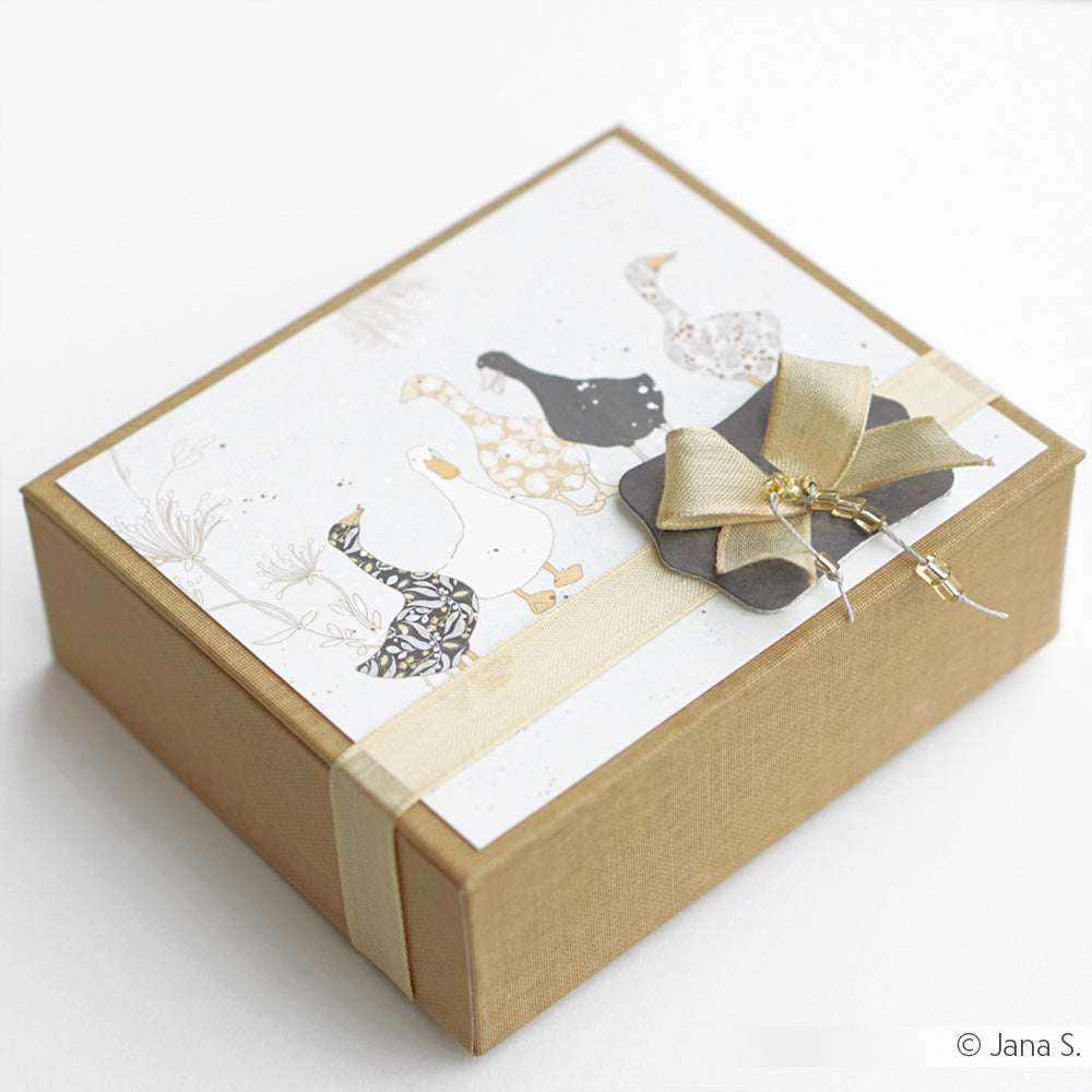 Goldfarbene Geschenkbox mit Schleife, mit Gänse-Illustrationen von Alexandra Renke - ideal für Papierprojekte oder um Designpapier-Flair in Ihre Buchbinderei zu bringen.