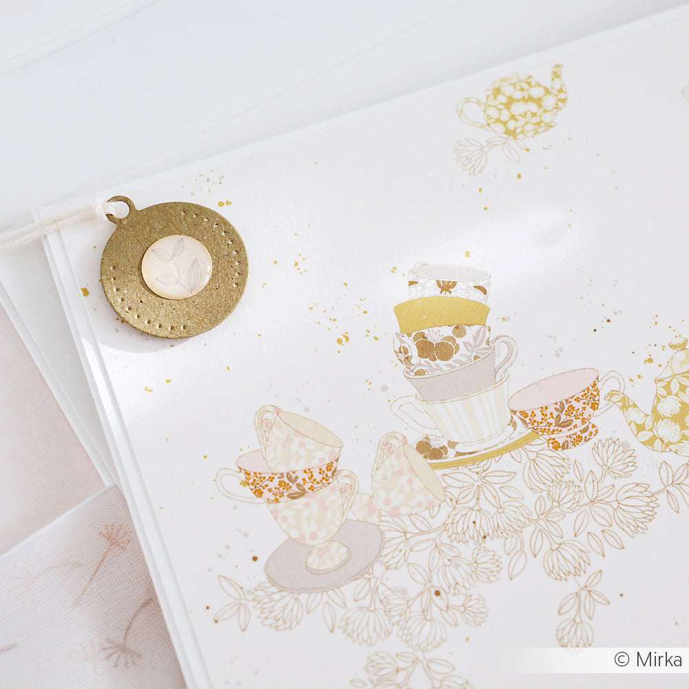 Gemusterte Teetassen- und Teekannen-Illustration von Alexandra Renke mit rundem goldenem Lesezeichen an der Seitenecke - ideal für Papierprojekte oder als Designpapier.