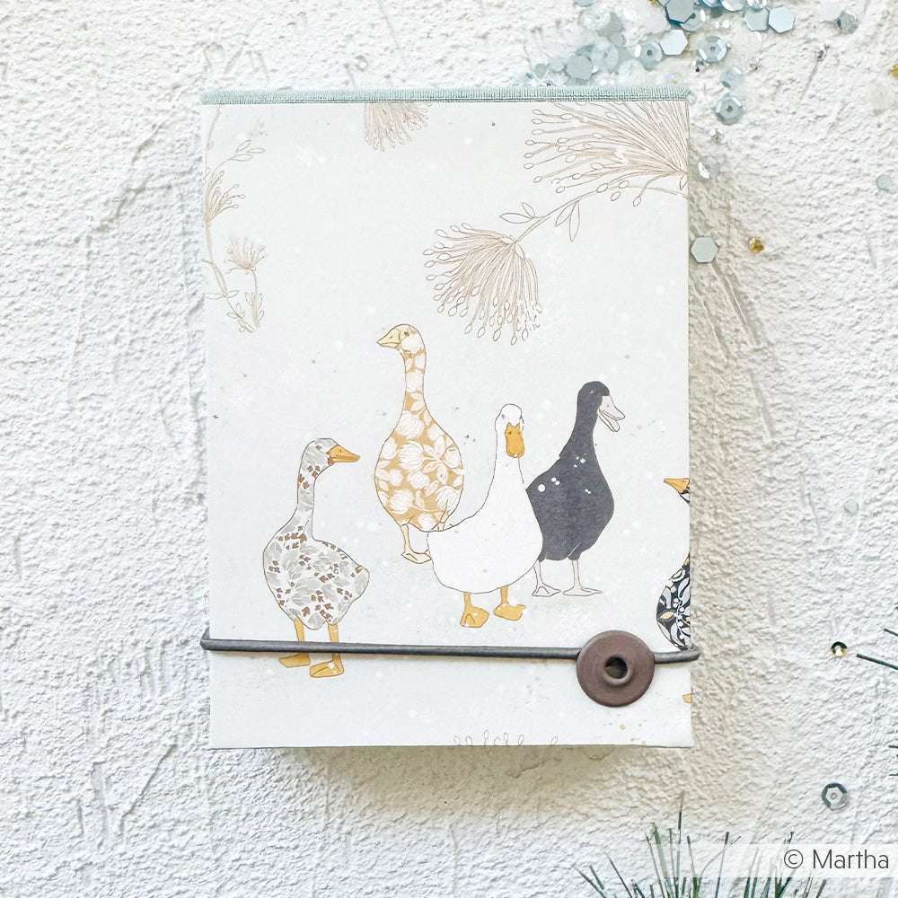 Ein Alexandra Renke Notizbuch mit illustrierten Enten auf dem Einband, gesichert mit einem Gummiband und Knopf - perfekt für Papierprojekte oder alle, die Wert auf einzigartige Buchbinderei legen.