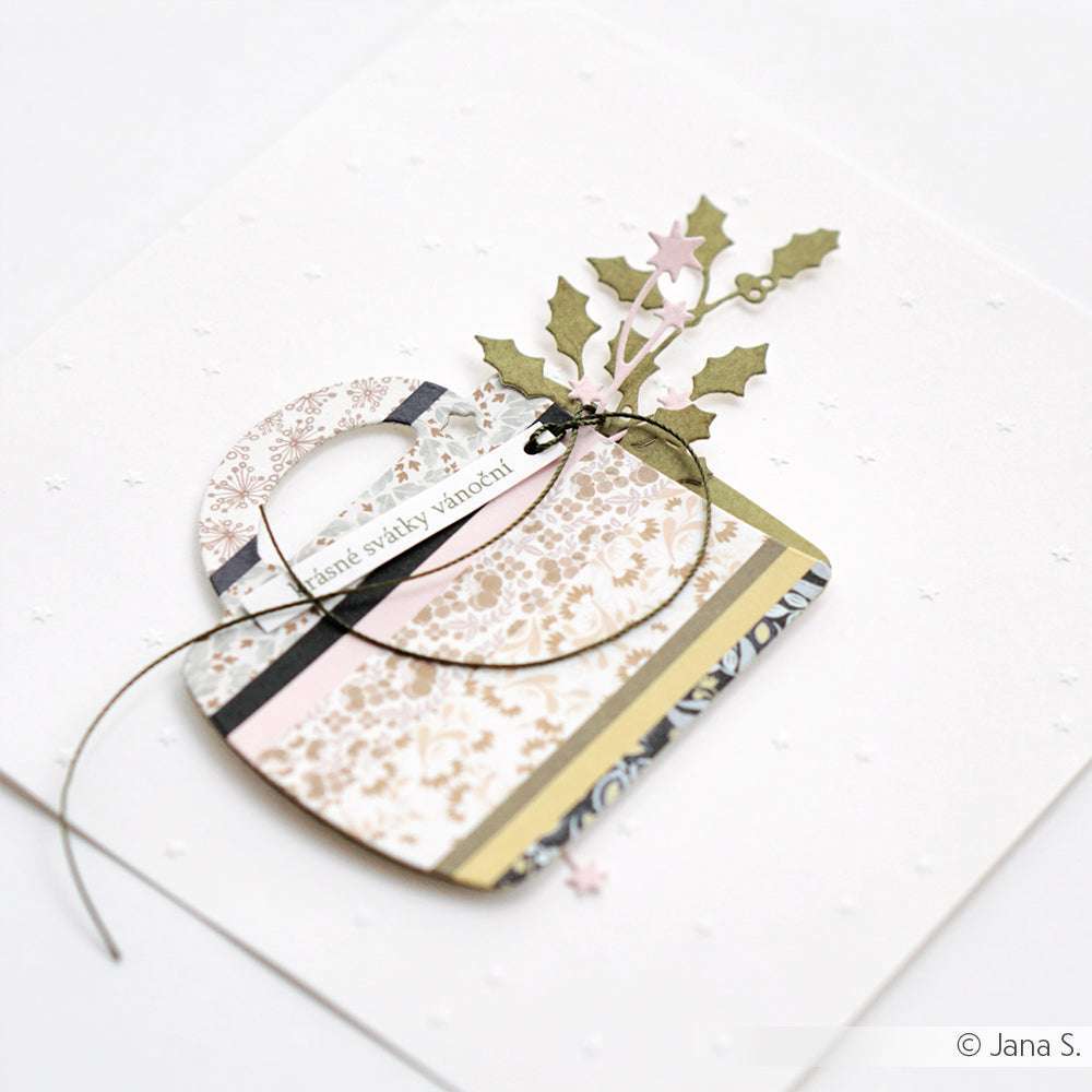 Handgemachte Karte mit einer dekorativen Papiertasche aus Designpapier von Alexandra Renke, Stechpalmenblättern und einer Kordelschleife auf weißem, strukturiertem Hintergrund - eine charmante Note für Ihre Papierprojekte.