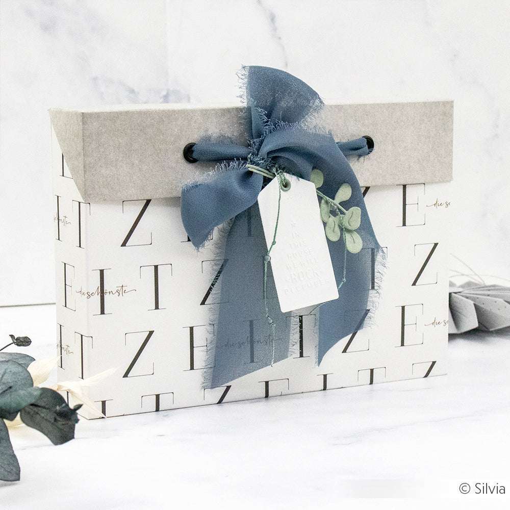 Alexandra Renke-Geschenkbox mit blauem Band, Blattakzent und Anhänger - ideal für Papierprojekte oder zur Kombination mit Grußkarten - auf weißem Hintergrund mit minimalem Dekor.