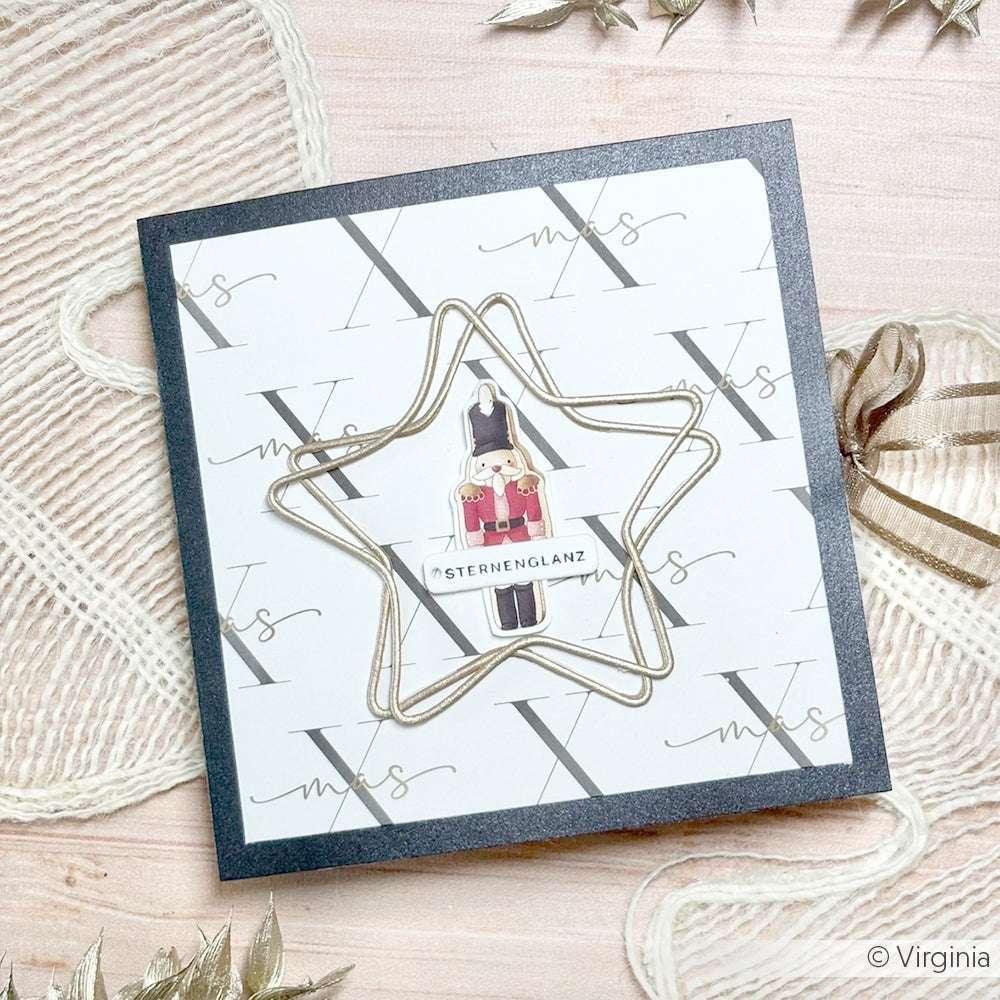 Die quadratische Weihnachtskarte von Alexandra Renke ist mit einem goldenen Stern, einer kleinen Nussknacker-Illustration und dem Text "Sternenglanz" versehen - ideal für Papierprojekte oder zum Auslegen Ihres Lieblingsdesignpapiers.