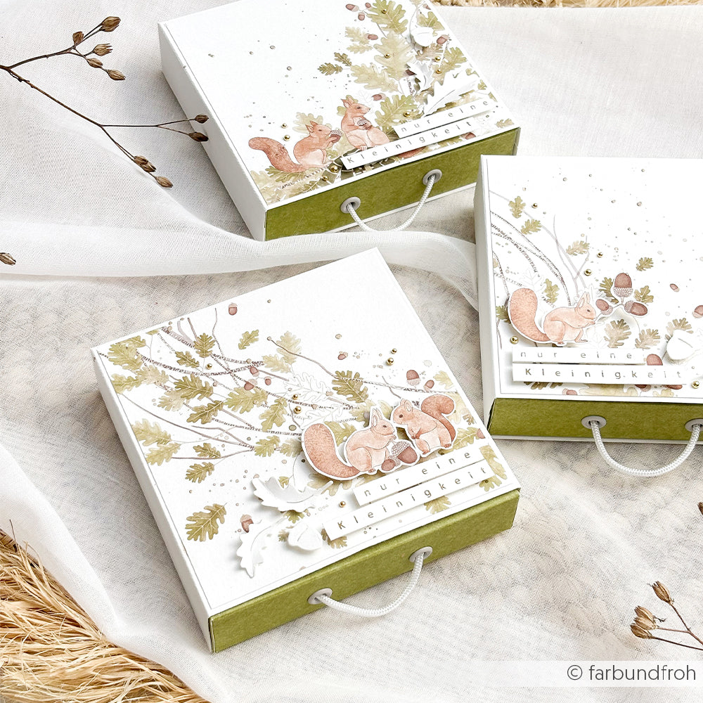 Drei kleine weiße Geschenkboxen aus Designpapier mit Eichhörnchen-Motiven.
