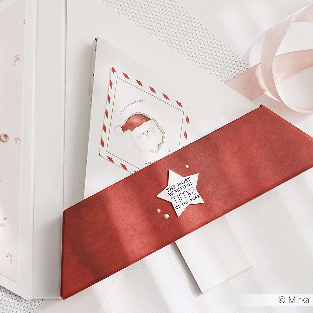 Roter Umschlag und Karte mit einem Weihnachtsmann-Sticker von Alexandra Renke auf weißem Untergrund, dazu rosa Schleife - ideal für festliche Papierprojekte oder als Inspiration für stilvolle Designpapier-Kreationen.