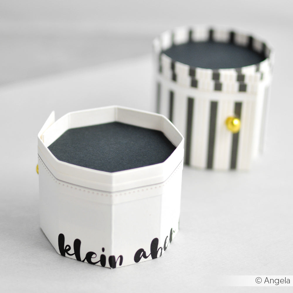 Zwei achteckige Papierschachteln von Alexandra Renke - eine gestreift, eine mit Text -, die jeweils mit einem kleinen goldenen Knopf versehen sind. Ideal für die Aufbewahrung von Grußkarten oder Papierprojekten.