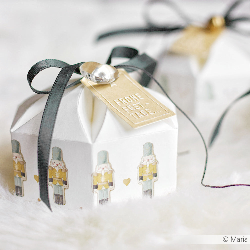 Kleine weiße Geschenkbox von Alexandra Renke mit Zinnsoldaten-Illustrationen, schwarzem Band und einem goldenen Anhänger - ideal für Papierprojekte oder als charmante Verpackung für Grußkarten.
