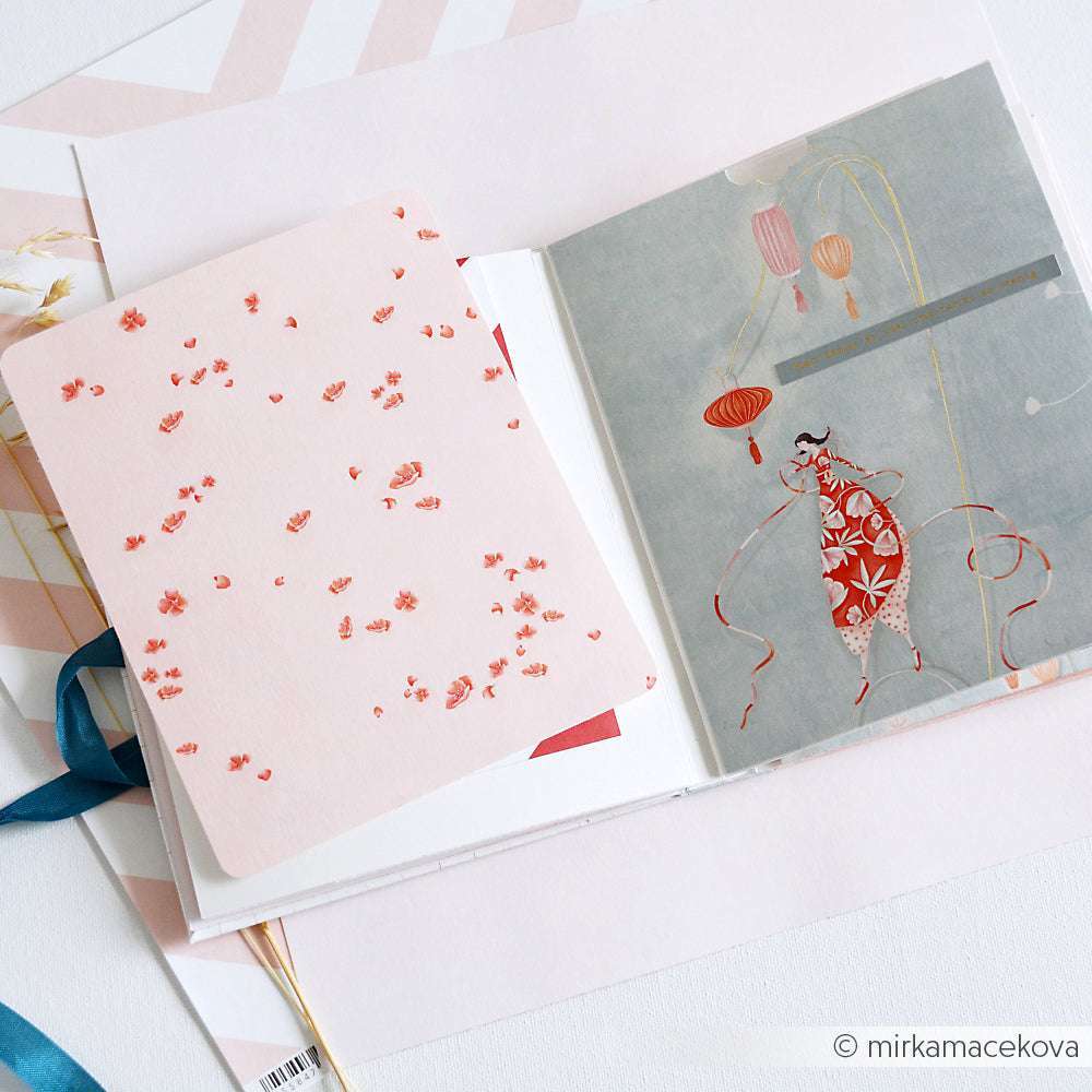 Aufgeschlagenes Alexandra Renke Notizbuch mit einer rosafarbenen floralen Designpapier-Seite und einer rechtsseitigen Illustration einer Frau mit Laternen - ideal für einzigartige Buchbinderei oder inspirierende Papierprojekte.