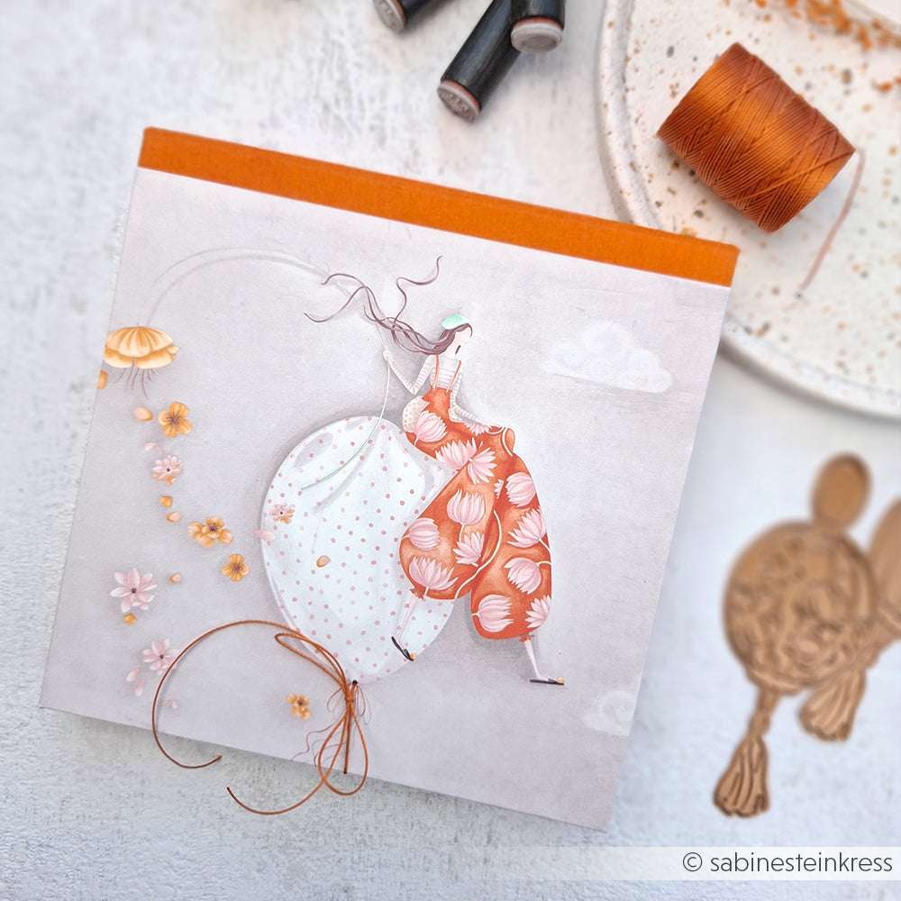 Ein Grußkarten-Design von Alexandra Renke mit zwei Frauen in Kleidern, orangefarbenem Faden und Nähzubehör auf weißem Designpapier - ideal für kreative Papierprojekte.