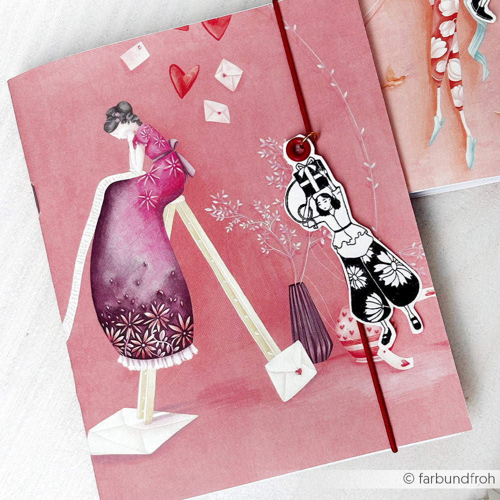 Alexandra Renke illustriertes Notizbuch mit rosa Designpapier, das eine Frau auf Stelzen und einen Akrobatenanhänger auf einem roten Band zeigt - ideal für Fans von Papierprojekten oder Buchbinderei.